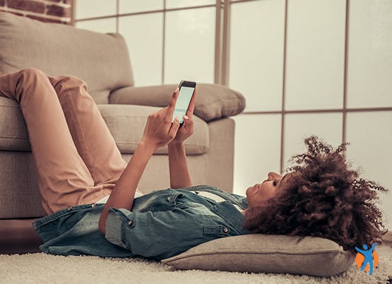 Femme allongée sur le sol avec ses jambes sur le canapé utilisant son smartphone