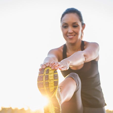 Femme souriante assise sur le sol à l'extérieur, étirant ses jambes après avoir fait de l'exercice