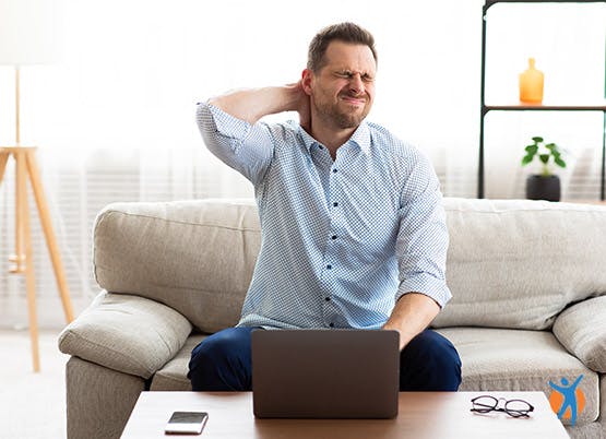 Un homme assis sur un canapé devant un ordinateur portable se tenait la nuque de douleur