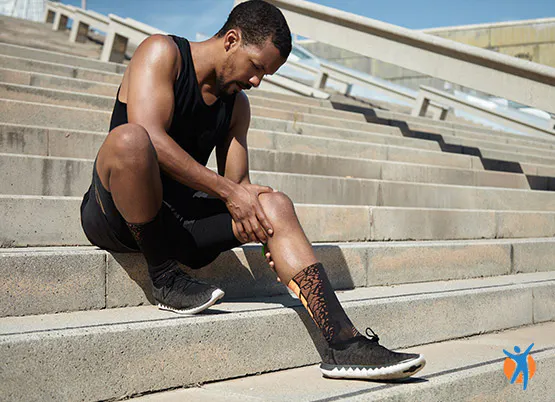 Homme en tenue de sport assis sur les marches à l'extérieur massant son genou pour soulager la douleur