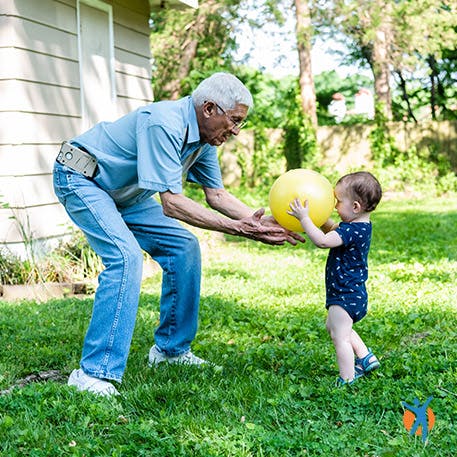 Avô e criança brincam no jardim, com bola.
