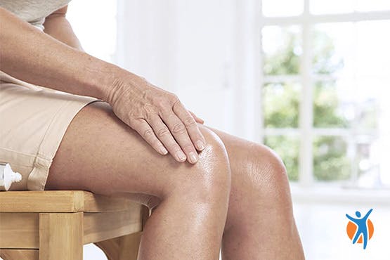 Mulher adulta exibe sinais de dor no joelho.