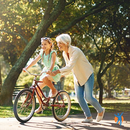Mãe e filha no parque, com a mãe a ajudar a mover a bicicleta.