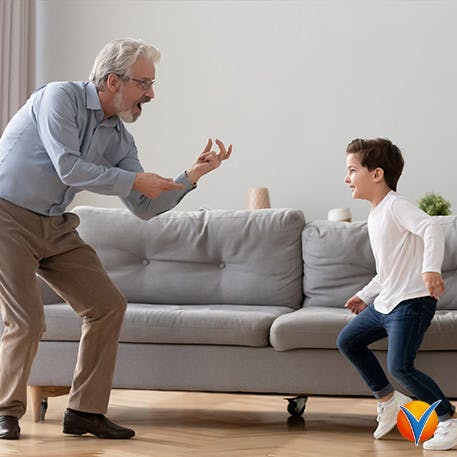 Äldre man leker med barnbarn hemma och böjer knäna fri från knäsmärta