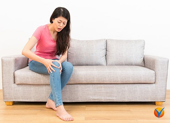 Kvinna sitter på soffan och håller om sitt knä på grund av knäsmärta