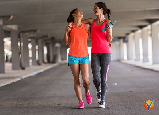 Två kvinnor håller om varandra och skrattar medan de tränar utomhus för att hålla sig i form