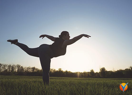 Kvinna som utövar yogaställning utomhus i ett fält vid skymning