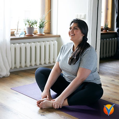 En ung kvinna ler medan hon sitter på sin yogamatta hemma