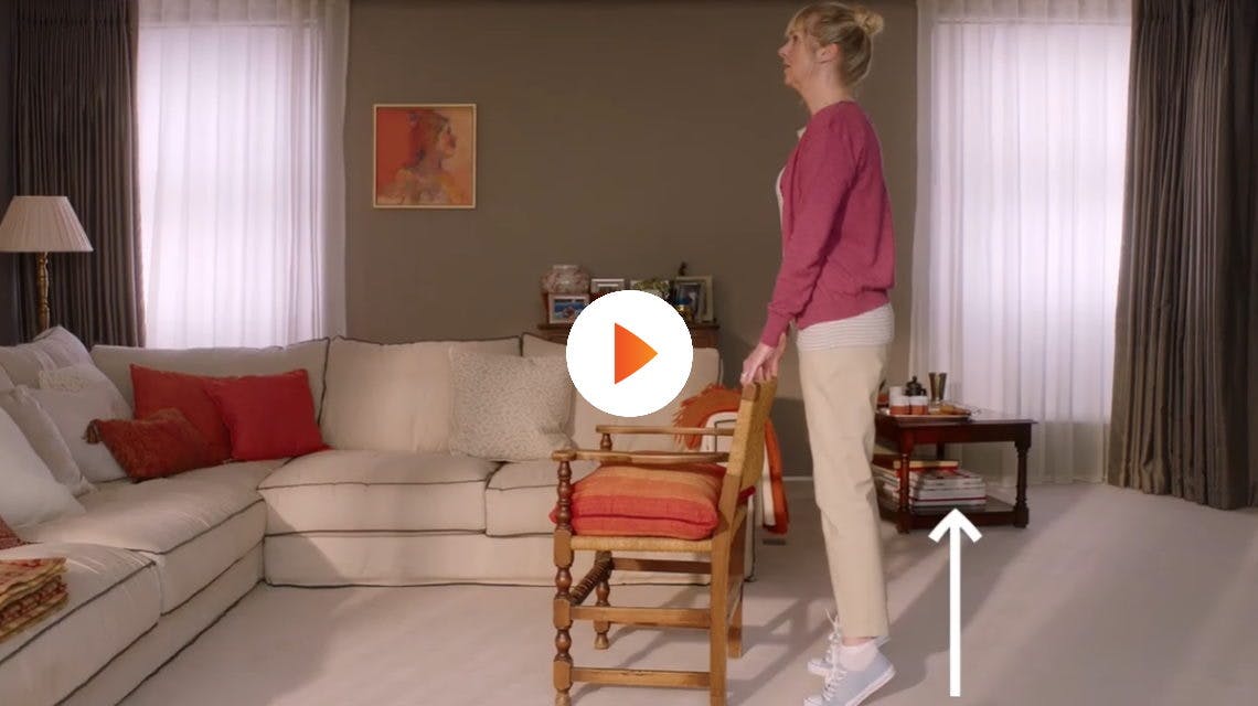 Kvinna gör knäövningar i vardagsrummet med en stol