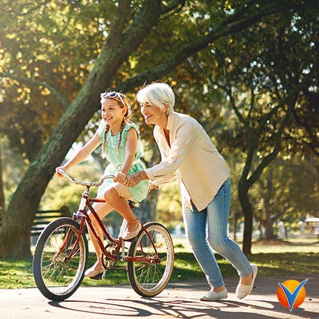 Äldre dam lär barnbarn att cykla i parken