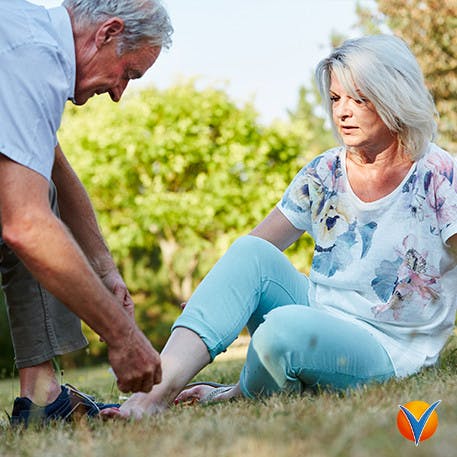 Äldre man hjälper äldre kvinna med hennes skadade fotled