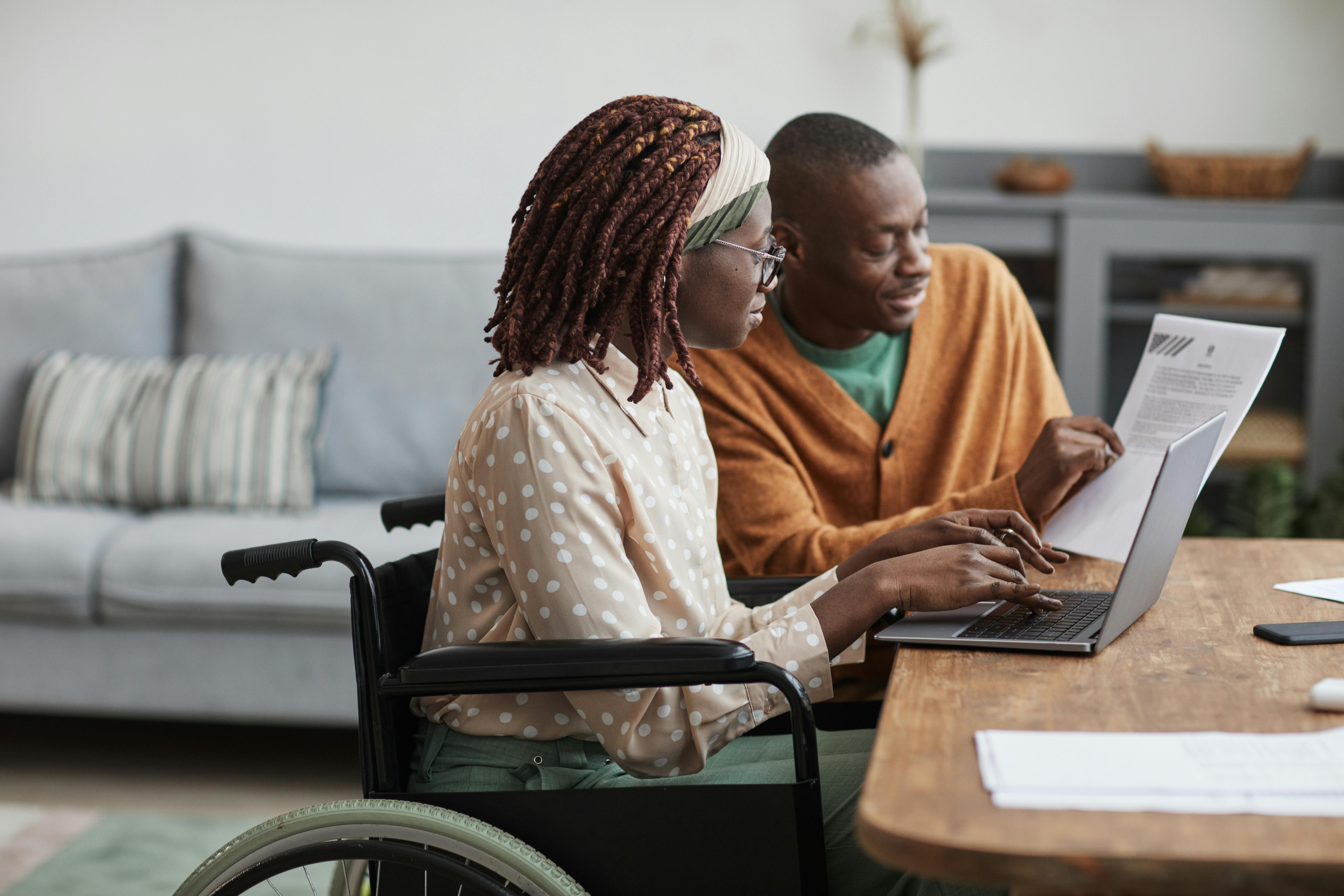 young woman in wheelchair on laptop speaking to her spouse