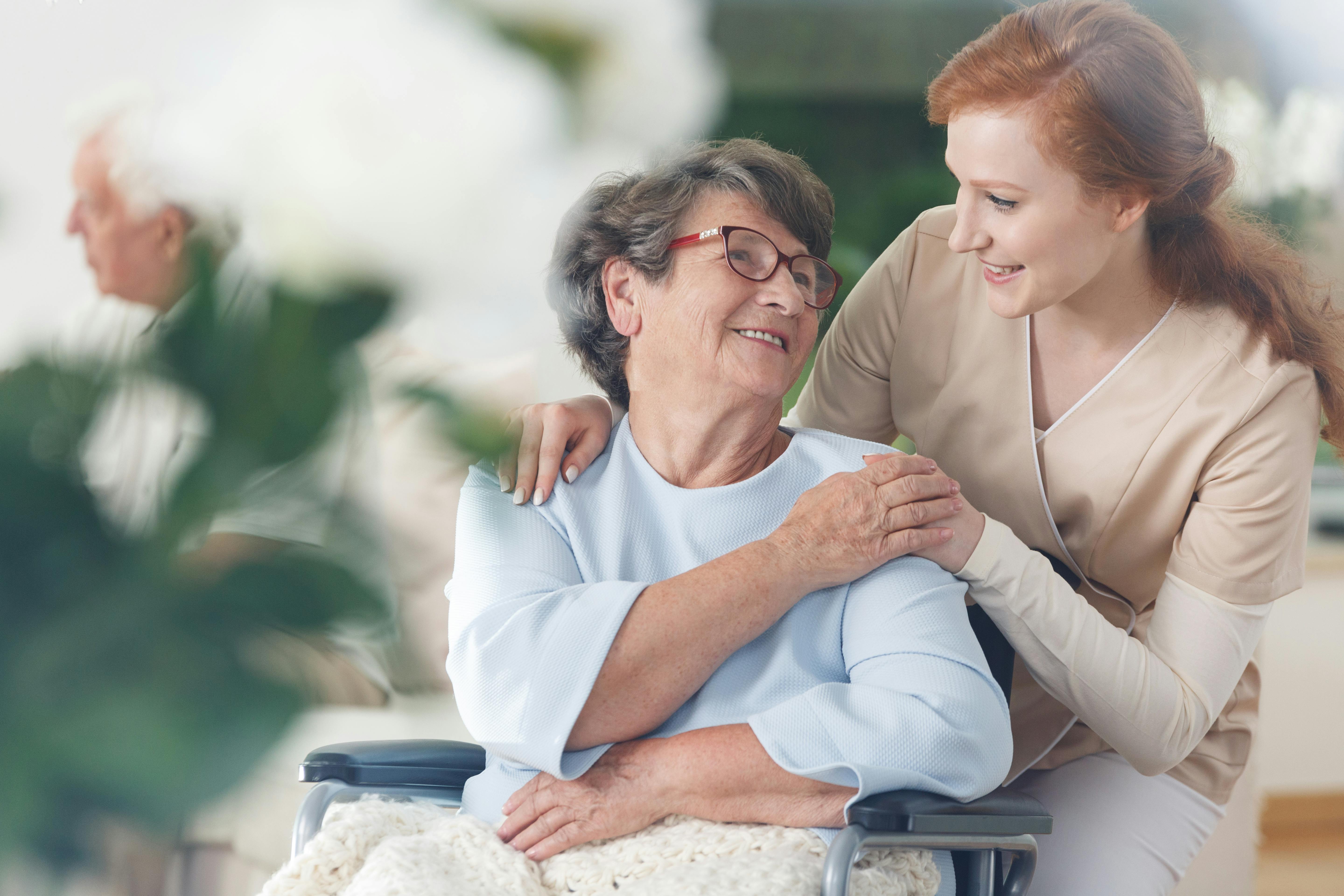 Elderly woman in a wheelchair and her caretaker smile together