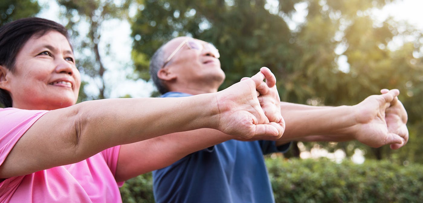 Older Asian couple stretching their arms and hands outside