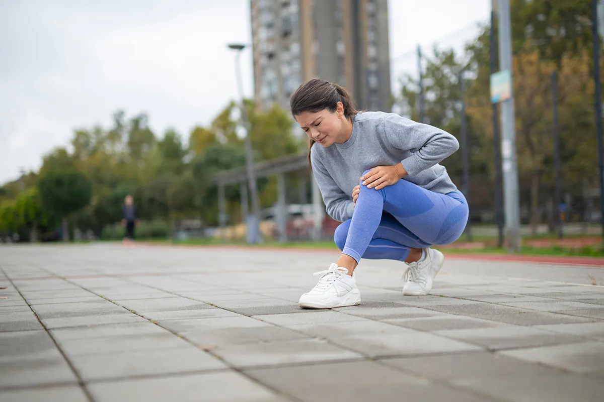 Woman outside in running clothes stooping down to grab her leg 