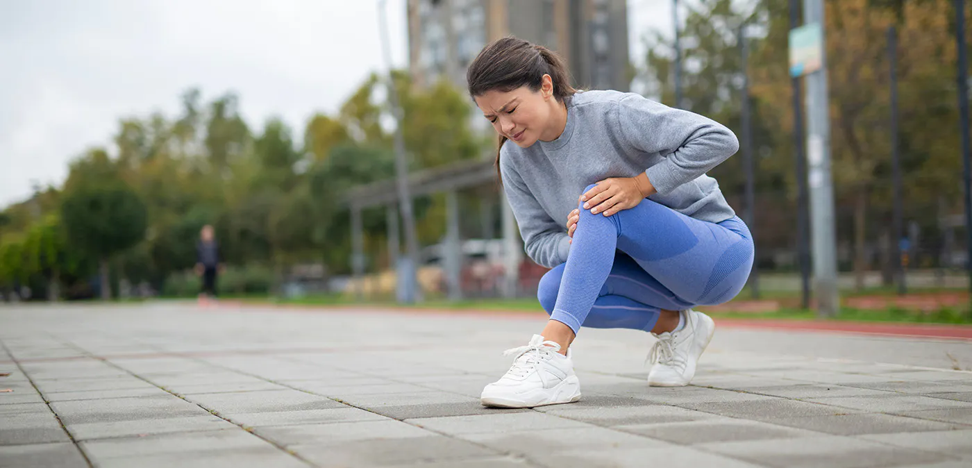 Woman outside in running clothes stooping down to grab her leg 