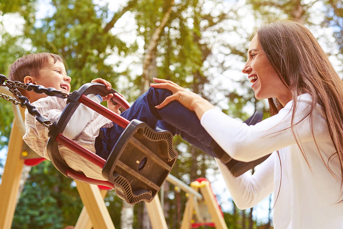 Brunette mother with her young son swinging on a swingset