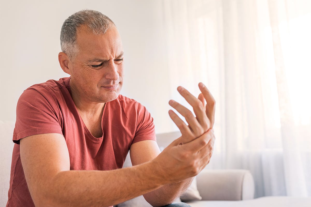 A man with a brown T-shirt has pain in his hand