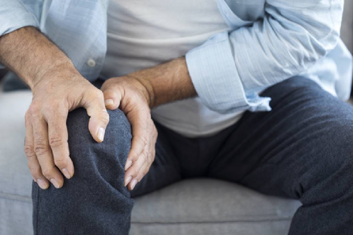 Older man sitting on sofa and holding his knee.