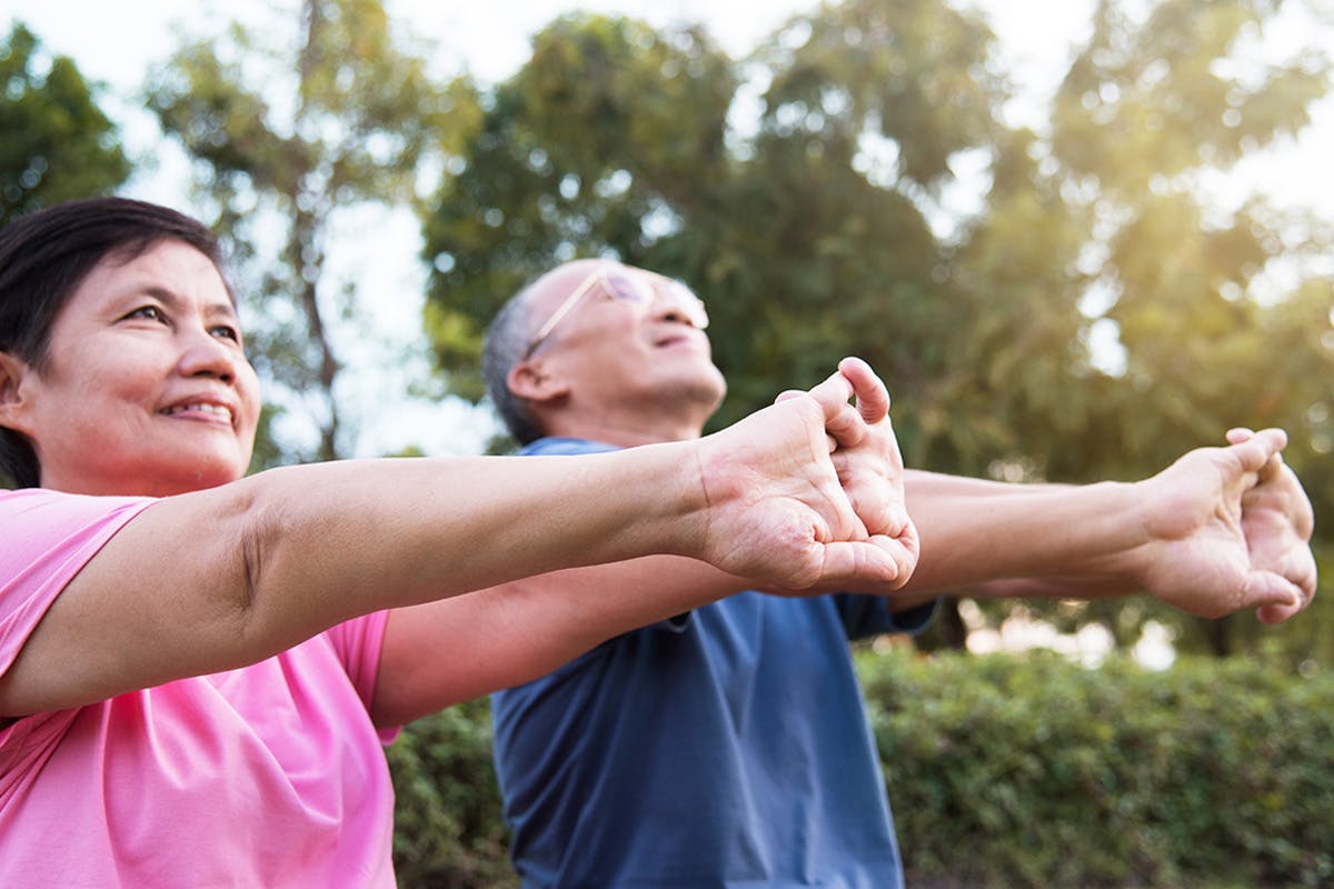 Older Asian couple stretching their arms and hands outside