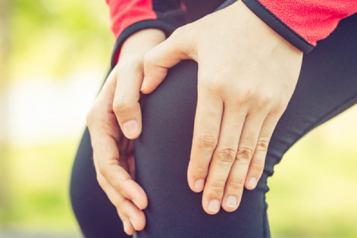 Close-up of female runner with her hands placed on her painful knee