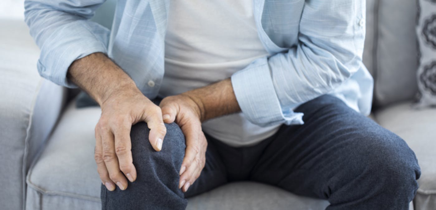 Older man sitting on sofa and holding his knee. 