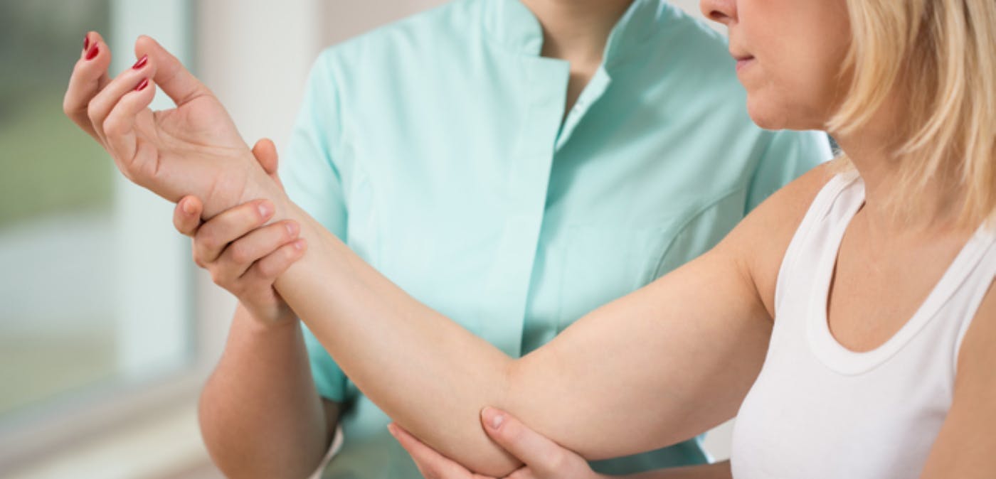 Older blonde woman experiencing elbow pain while physical therapist examines