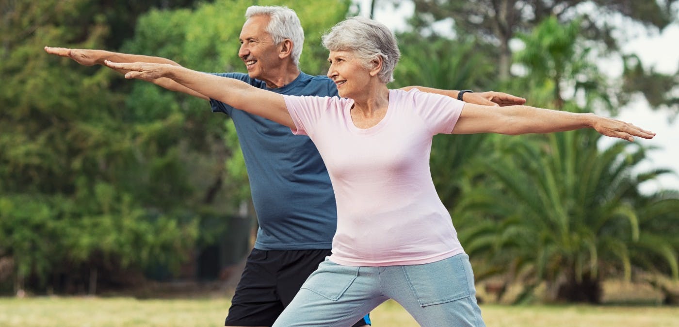 an elderly couple doing yoga poses outside