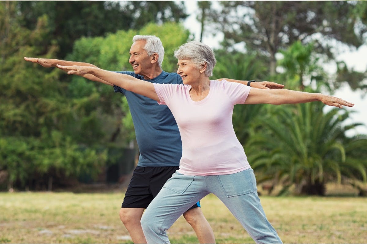 an elderly couple doing yoga poses outside