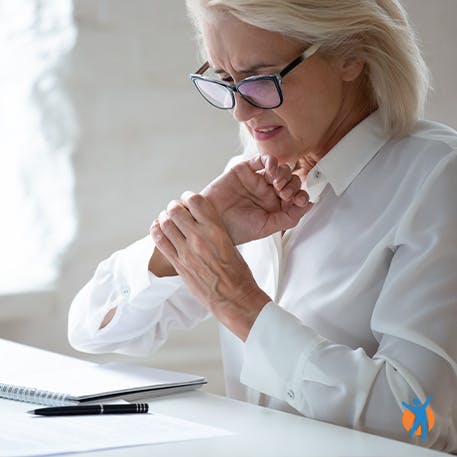 Woman at desk holding her wrist - learn about the causes of pain in the wrists