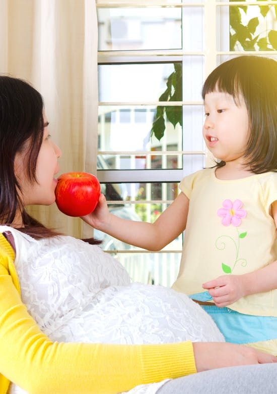 妊娠中の母親にりんごを差し出す幼い女の子 妊娠中の母親にりんごを差し出す幼い女の子