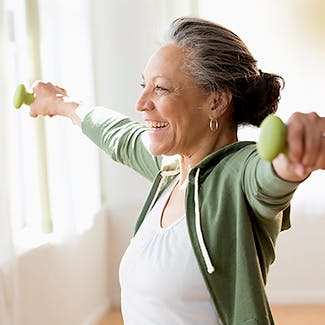 Eldre kvinne trener armene med lette manualer.