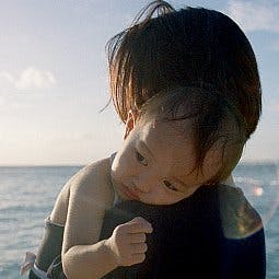 Małe dziecko na ramionach swojej mamy na tle morza