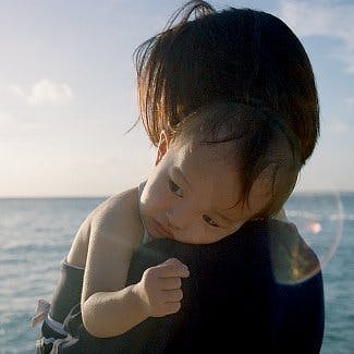 Małe dziecko na ramionach swojej mamy na tle morza