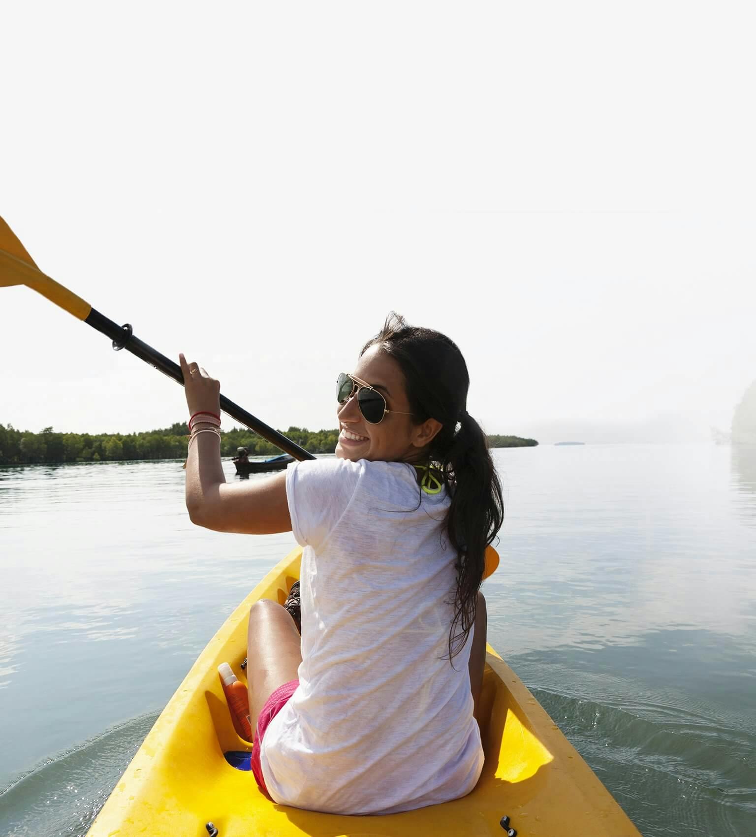 Uśmiechnięta dziewczyna w okularach przeciwsłonecznych płynąca na kajaku przez jezioro