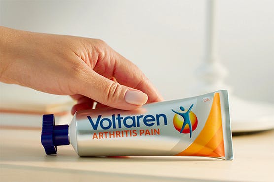 una imagen de la mano femenina sosteniendo el tubo de Voltaren Arthritis Pain sobre el fondo claro