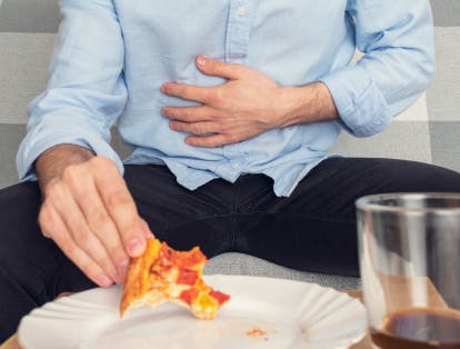 Homme tenant d’une main un morceau de pizza et portant l’autre main à l’estomac