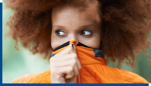 Woman in orange coat covering her face due to cold sores