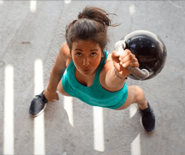 Stående kvinne med kettlebell løftet over hodet, avbildet ovenfra